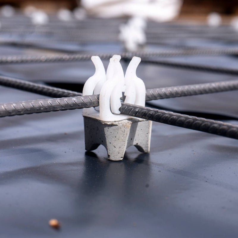 Concrete spacers with plastic clips for securing rebar and mesh using four-point support system for minimal formwork contact 