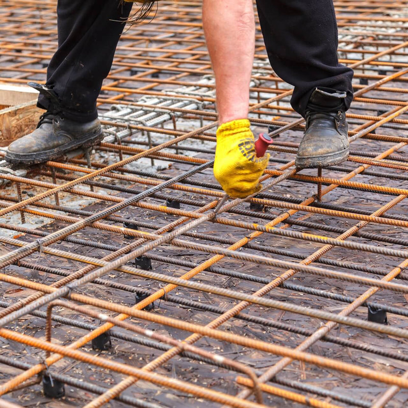 A worker ties reinforcing steel bars with a tying wire on a construction site