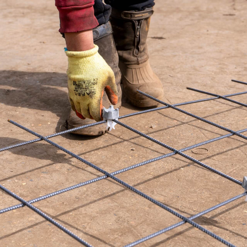 Builder placing concrete spacer clips on mesh for secure rebar support and proper alignment during construction.