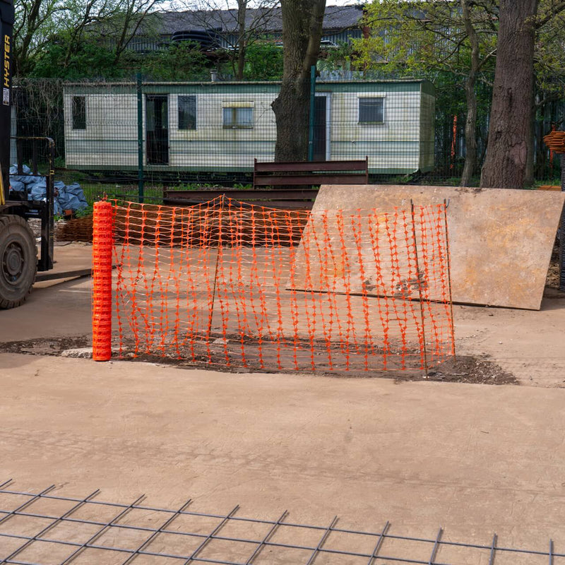 Bright orange temporary fencing mesh encloses a work zone for safety